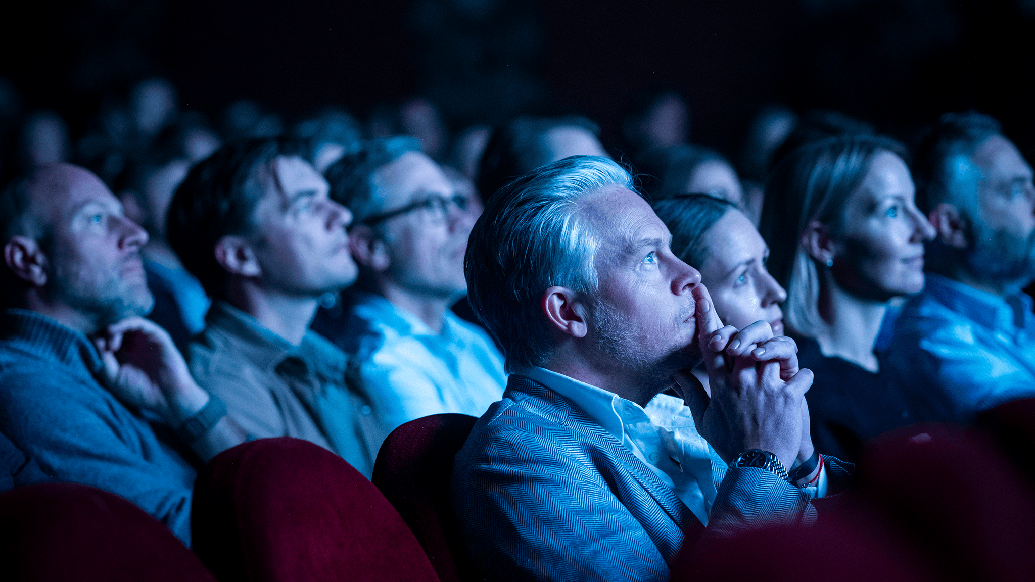 Audience members watching attentively at EICON, lit by blue stage lighting at Chinateatern.