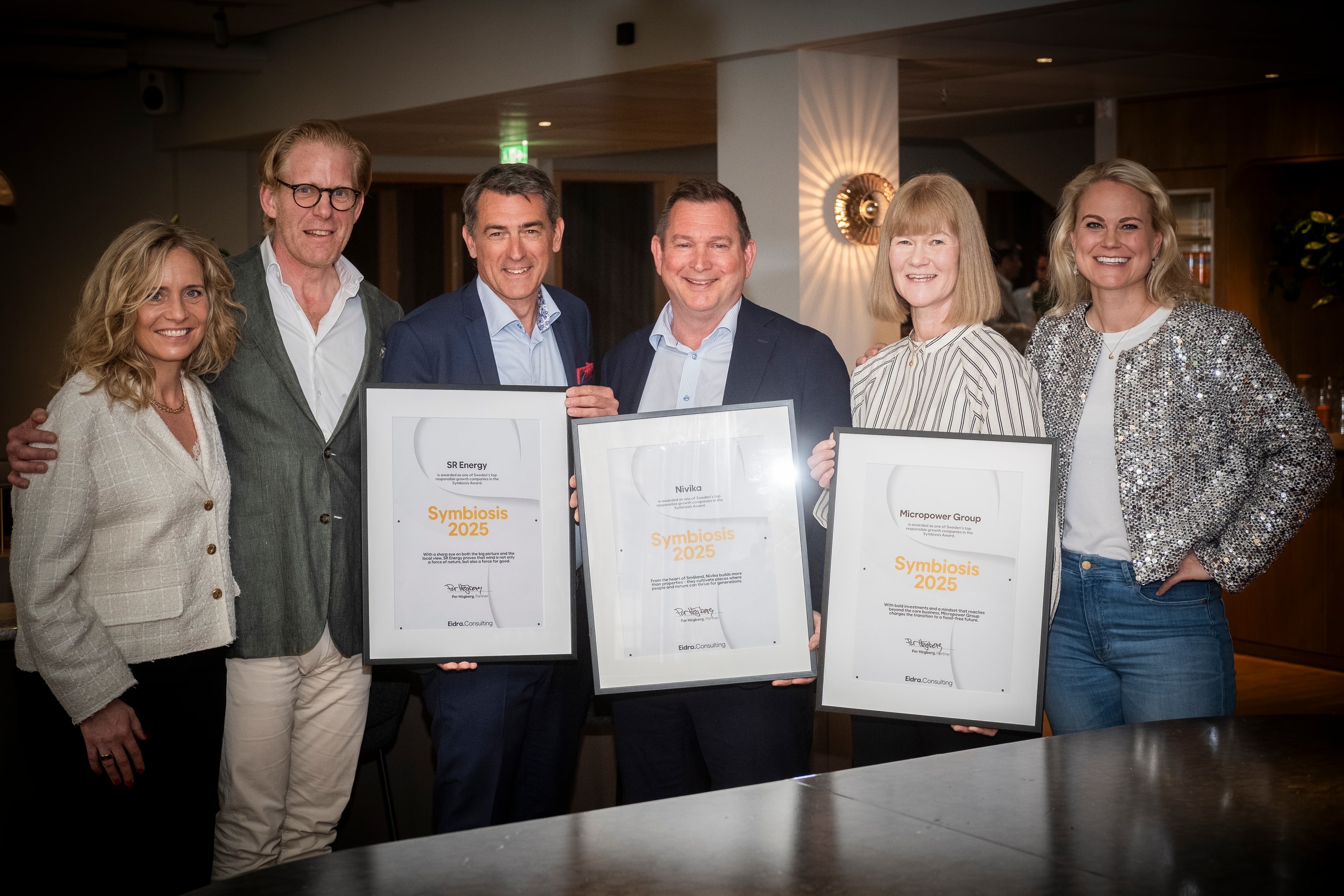 Six people standing in a row with diplomas