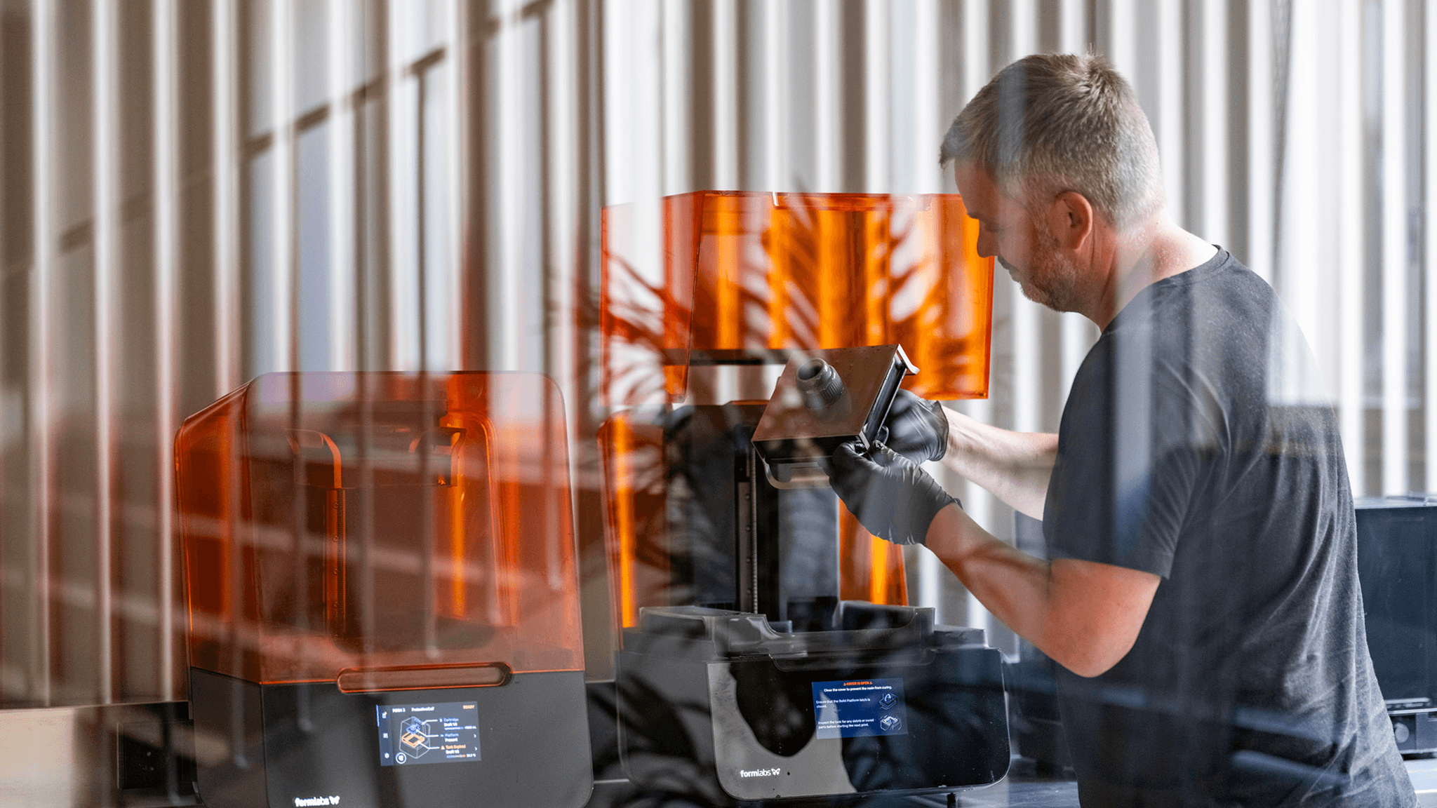 A person wearing black gloves removing a print from a resin 3D printer in an Eidra workspace.