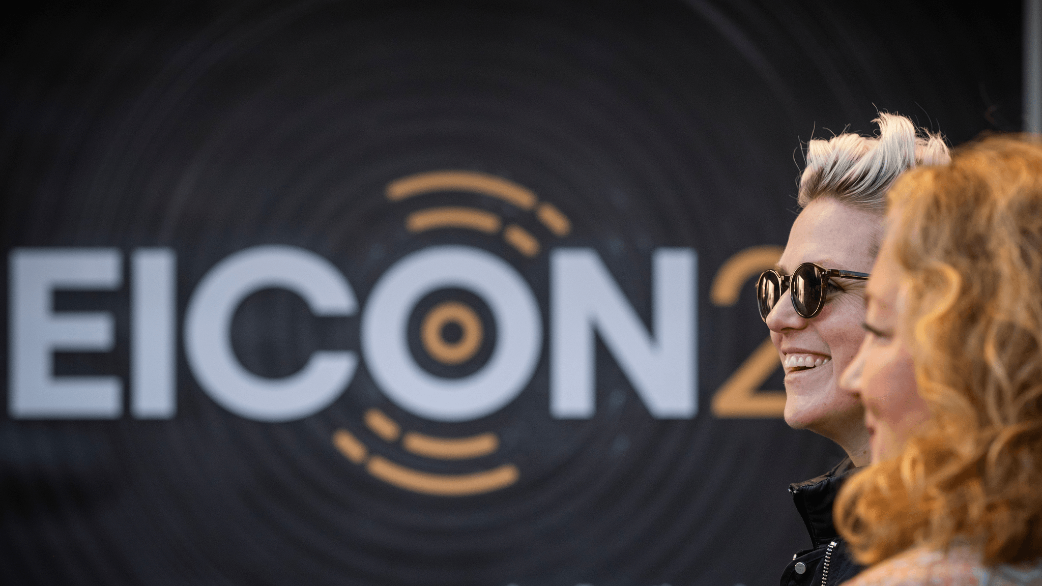 Two attendees smiling in front of the EICON25 event backdrop outside Chinateatern.
