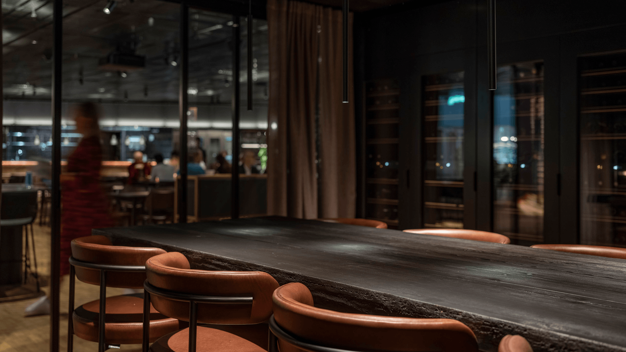 The wine room at Eidra's office, featuring a dark wood counter with tan leather bar stools, with views through glass doors into the piazza beyond.